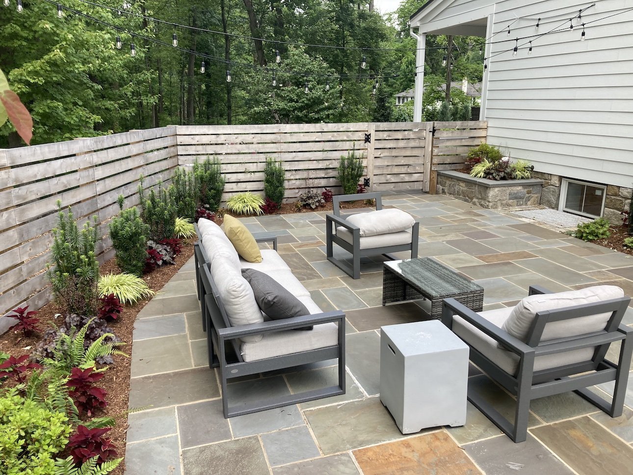 Outdoor patio area for all weather lounging with fence and patio furniture surrounded by lush greenery landscaping.jpg